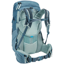 Load image into Gallery viewer, Angled back panel view of the blue backpack showing the shoulder straps&#39; top and waist belts locked. 
