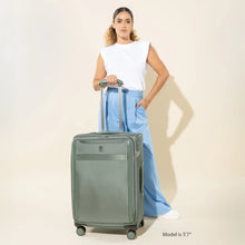 Load image into Gallery viewer, A young woman posing while holding the green suitcase by the extended telescopic handle. 
