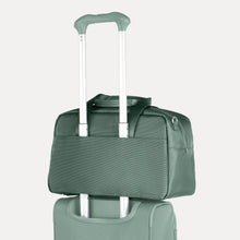 Load image into Gallery viewer, Back panel view of a green suitcase&#39;s telescopic handle passing through the back strap of the bag to hold it in place. 
