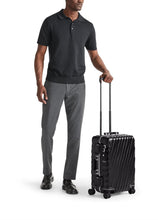 Load image into Gallery viewer, A young man holding a black suitcase by the extended telescopic handle. Set on a white background. 
