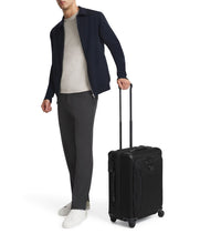 Load image into Gallery viewer, A young man holding the black suitcase by the extended telescopic handle.

