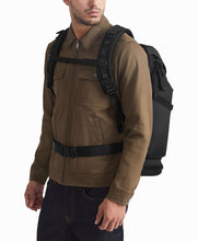 Load image into Gallery viewer, A model carrying the backpack with the attachment straps locked across his chest. 
