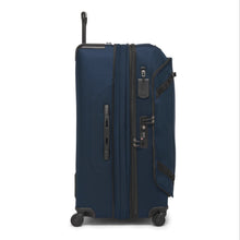 Load image into Gallery viewer, Side panel view of the blue soft sided suitcase with black accents. The expandable feature is unzipped. This side features a grab handle, a tag, and a TSA approved three-digit combination lock. 
