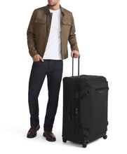 Load image into Gallery viewer, A young man holding the black suitcase by the extended telescopic handle on a white background. 
