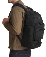 Load image into Gallery viewer, Side view of a man carrying the backpack on his shoulders. A tag is shown on the side panel. 
