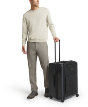 Load image into Gallery viewer, A young man holding his black suitcase by the extended telescopic handle.
