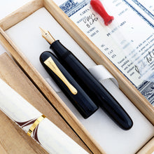 Load image into Gallery viewer, The image displays the Visconti Black Urushi fountain pen  without its cap, laying in its woden box surrounded by the included documents, and eyedropper. 
