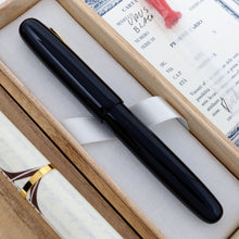 Load image into Gallery viewer, The image shows the side of the Visconti Black Urushi with its cap on, laying in its original box with the included items. 
