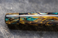 Load image into Gallery viewer, Close up to the bottom of the Visconti Earth Origins Pen. The lacquer is shimmering in aqua, yellow, and dark brown color swirls.
