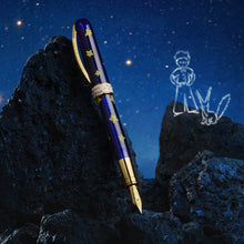 Load image into Gallery viewer, A decorative fountain pen with a deep blue barrel decorated with gold stars and gold trim, resting on dark rocks against a starry night sky background. A white line-art sketch of The Little Prince and a Fox stands to the right.
