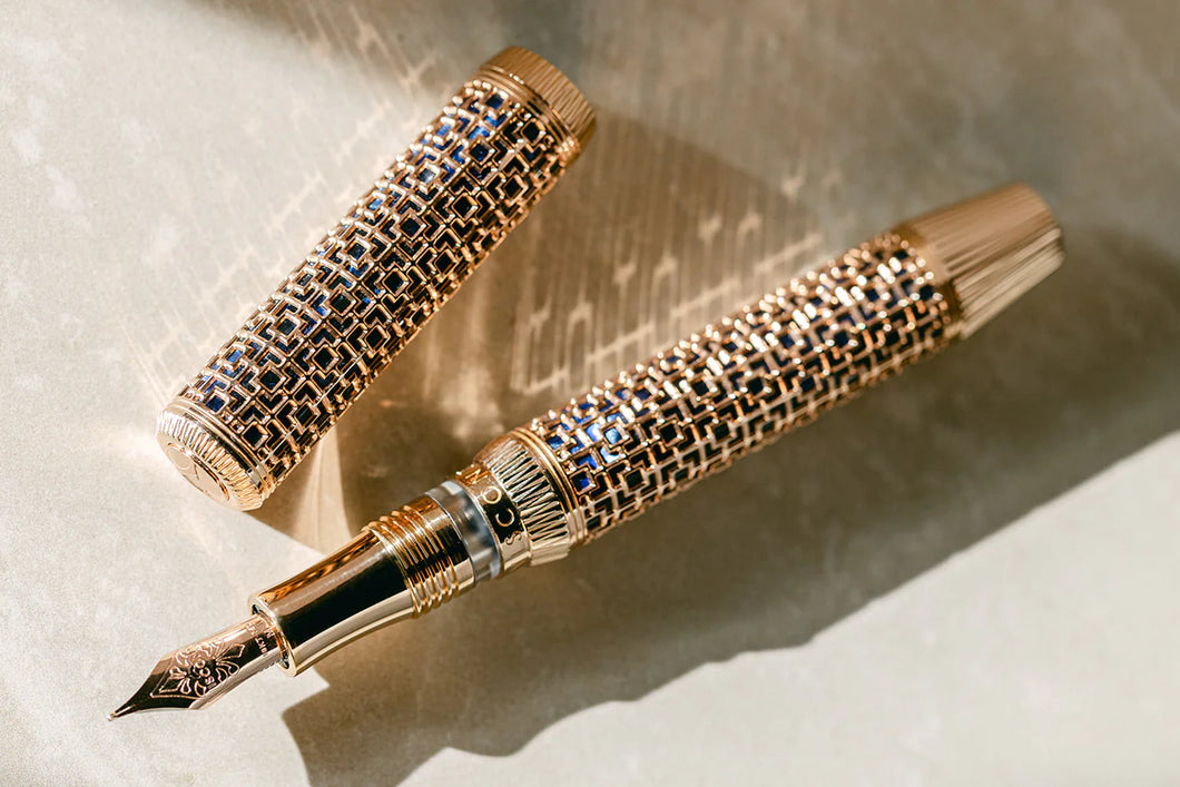 Front view of the Visconti Looking East Fountain Pen with the cap set to the side. It is a blue barrel covered in a golden overlay of square designs.  