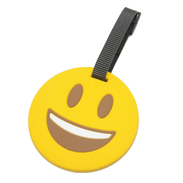 Angled front view of the luggage tag in the shape of a smile emoji. It has a black strap.