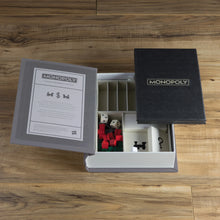 Load image into Gallery viewer, Open Monopoly game box with pieces and cards on a wooden surface
