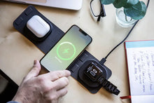 Load image into Gallery viewer, The charging station set on a desk while charging a cellphone, earbuds case, and smart watch.
