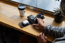 Load image into Gallery viewer, The charging station on a wooden board. A young woman reaches for the cellphone being charged on the station between the earbuds and smart watch.
