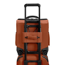 Load image into Gallery viewer, Back panel view of the canyon orange cabin spinner bag. The interlocking handle is attaching it to the extended handle of a suitcase.
