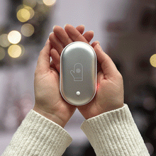 Load image into Gallery viewer, The image shows two hands holding the device on its hand-warming setting on a background of soft blurry holiday lights.
