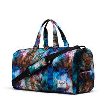 Load image into Gallery viewer, Angled front view of the Summer Tie Dye Novel Duffle bag. The grab handles are pulled up and a shoulder strap is laid across the front.

