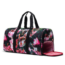Load image into Gallery viewer, Angled front view of the Pixel Floral Novel Duffle. The side panel show compartment is unzipped. 
