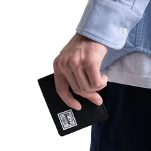Load image into Gallery viewer, Hand holding a black Roy wallet with a Herschel logo tag.
