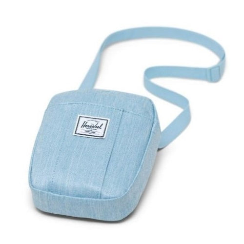 Angled view of the blue bag with the strap behind it. A Tag with the Herschel logo is sown on the front. Placed on a white background.
