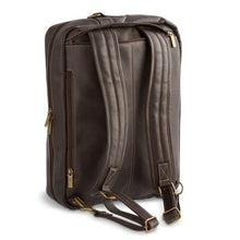 Load image into Gallery viewer, Angled back panel view of the brown leather backpack brief with the shoulder straps taken out of their zipper-closing pocket. 
