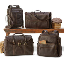 Load image into Gallery viewer, A brown leather briefcase, a duffle bag, and two backpacks arranged by a wooden bench with books and accessories on a white background. 
