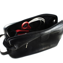 Load image into Gallery viewer, The black leather toiletry bag, opened. A pair of scissors and a USB cable are stored inside. 
