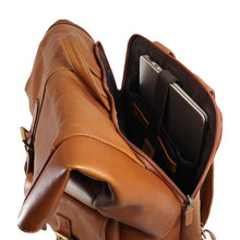 Load image into Gallery viewer, Angled view of the tan leather backpack. The back panel pocket is unzipped with a laptop stored inside. 
