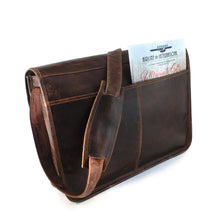 Load image into Gallery viewer, Angled back panel view of the brown leather messenger bag. The matching adjustable strap is draped across. A catalog is stored inside the pocket. 
