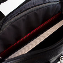 Load image into Gallery viewer, Angled close up to the black leather briefcase interior. A red laptop and a book are stored inside. 
