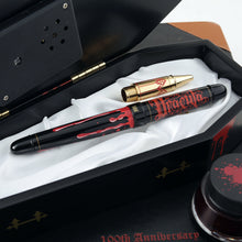 Load image into Gallery viewer, View of the pen with the cap on. It is set on the coffin-shaped presentation box with the rollerball attachment set next to it. There is an ink bottle next to the box.
