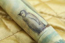 Load image into Gallery viewer, Close up to the baby penguin painted next to the larger one on the barrel. Placed on top of a golden fabric.
