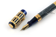 Load image into Gallery viewer, Close up to the fountain pen&#39;s nib with the cap placed on the side. The body and cap are made of blue marbled resin with golden trims. Set on a white background
