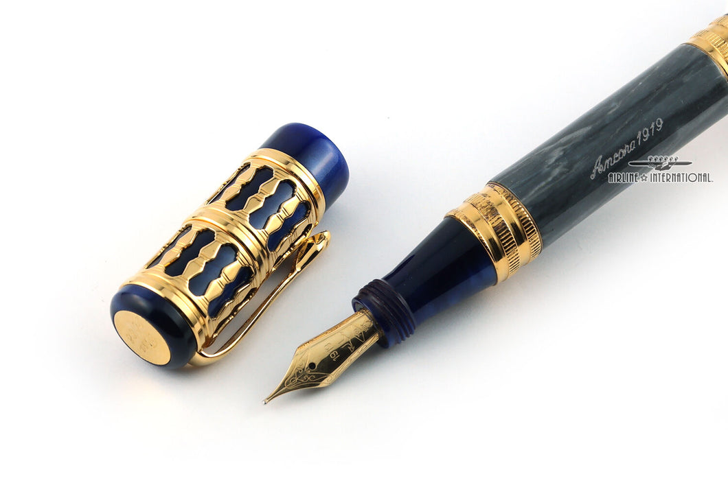 Close up to the fountain pen's nib with the cap placed on the side. The body and cap are made of blue marbled resin with golden trims. Set on a white background