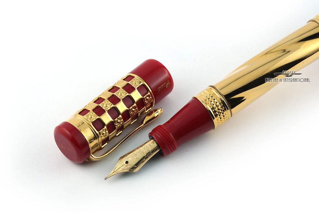 Close up to the Fountain pen nib with the cat placed to the side. Set on a white background. The pen is made of red marbled resin with the cap and the barrel having a gold-plated design. 