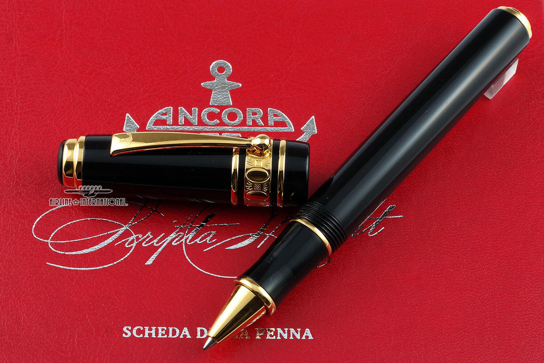 The pen with the cap set to the side. Both items are placed on top of the red document that's included. The pen is black with yellow-gold colored trims.