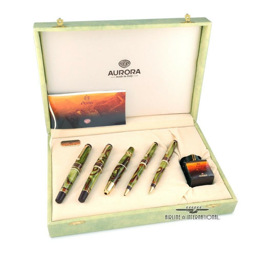 View of the five writing instruments and the ink bottle in the presentation box. Set on a white background. The pens are made of a combination of green and brown resin swirls with gold-plated accents.
