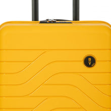 Load image into Gallery viewer, Close up to the top front of the mango yellow hard shell suitcase. The wave lines design is visible with the circular black BY logo at the top right.
