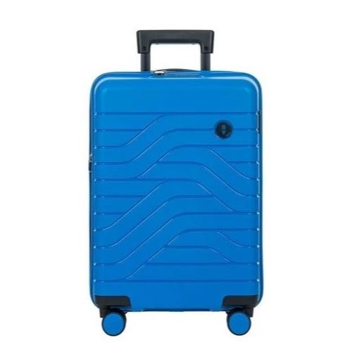 Front view of the electric blue hard shell suitcase with black accents. The panel has a textured wave lines design, and a small black circular logo at the top right. The telescopic handle is partly pulled.
