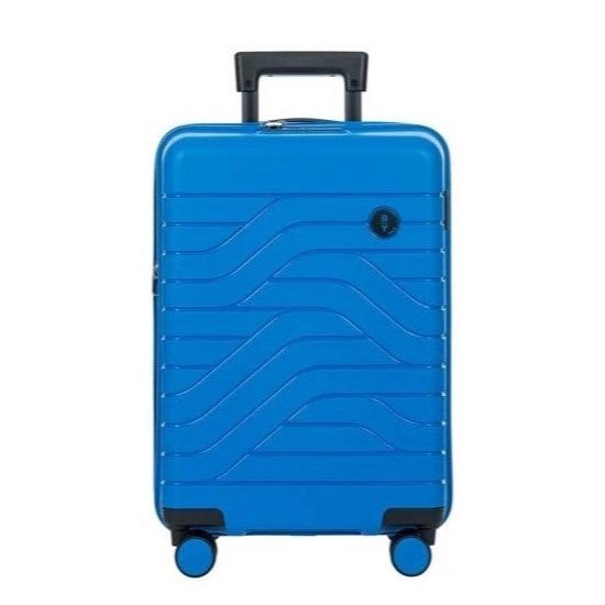 Front view of the electric blue hard shell suitcase with black accents. The panel has a textured wave lines design, and a small black circular logo at the top right. The telescopic handle is partly pulled.
