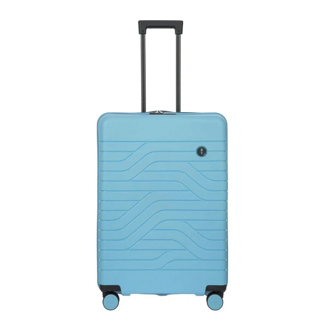 Front view of the light blue hard shell suitcase with black accents. The panel has a textured wave lines design, and a small black circular logo at the top right. The telescopic handle is pulled up.