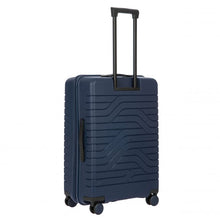 Load image into Gallery viewer, Angled back view of the navy blue  hard shell suitcase with black accents. The back panel has a textured wave lines design. The telescopic handle is pulled up.
