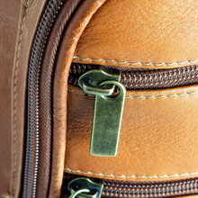 Load image into Gallery viewer, Close up to a brass zipper pull on the tan leather backpack. 
