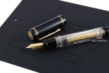 Load image into Gallery viewer, Angled view of the fountain pen with the cap set next to it. Both are laid on top of the included booklet. 
