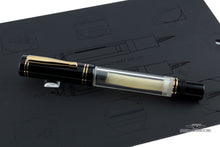 Load image into Gallery viewer, Angled view of the fountain pen with the cap on. Set on top of the a black booklet with outlined illustrations of the pen.
