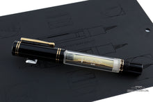 Load image into Gallery viewer, Side view of the fountain pen with the cap on. Set on top of a black booklet with outlined illustrations of the pen. 
