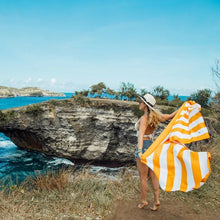 Load image into Gallery viewer, A young woman wearing a hat holds the white and orange stripes towel behind her on a lake setting.
