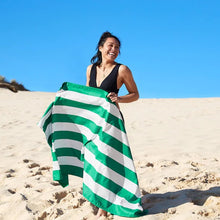 Load image into Gallery viewer, A young smiling woman walking on beach sand while holding the green and white towel in front of her.

