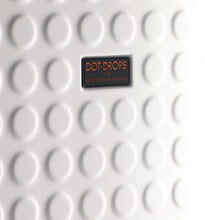 Load image into Gallery viewer, Close up to the Dot Drops logo badge on the front panel of the white suitcase. 
